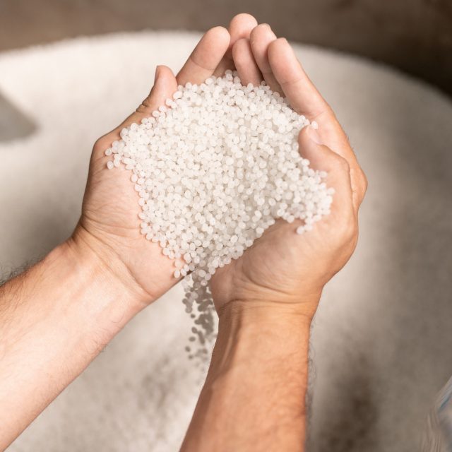 View of modern factory worker hands holding pile of white polymer pellets